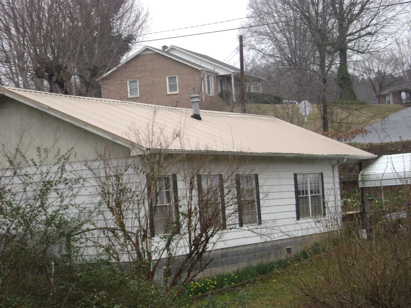 Tan metal roof on a white sided house set into a hillside — Commercial Roofing by Roofing Brothers in Birmingham