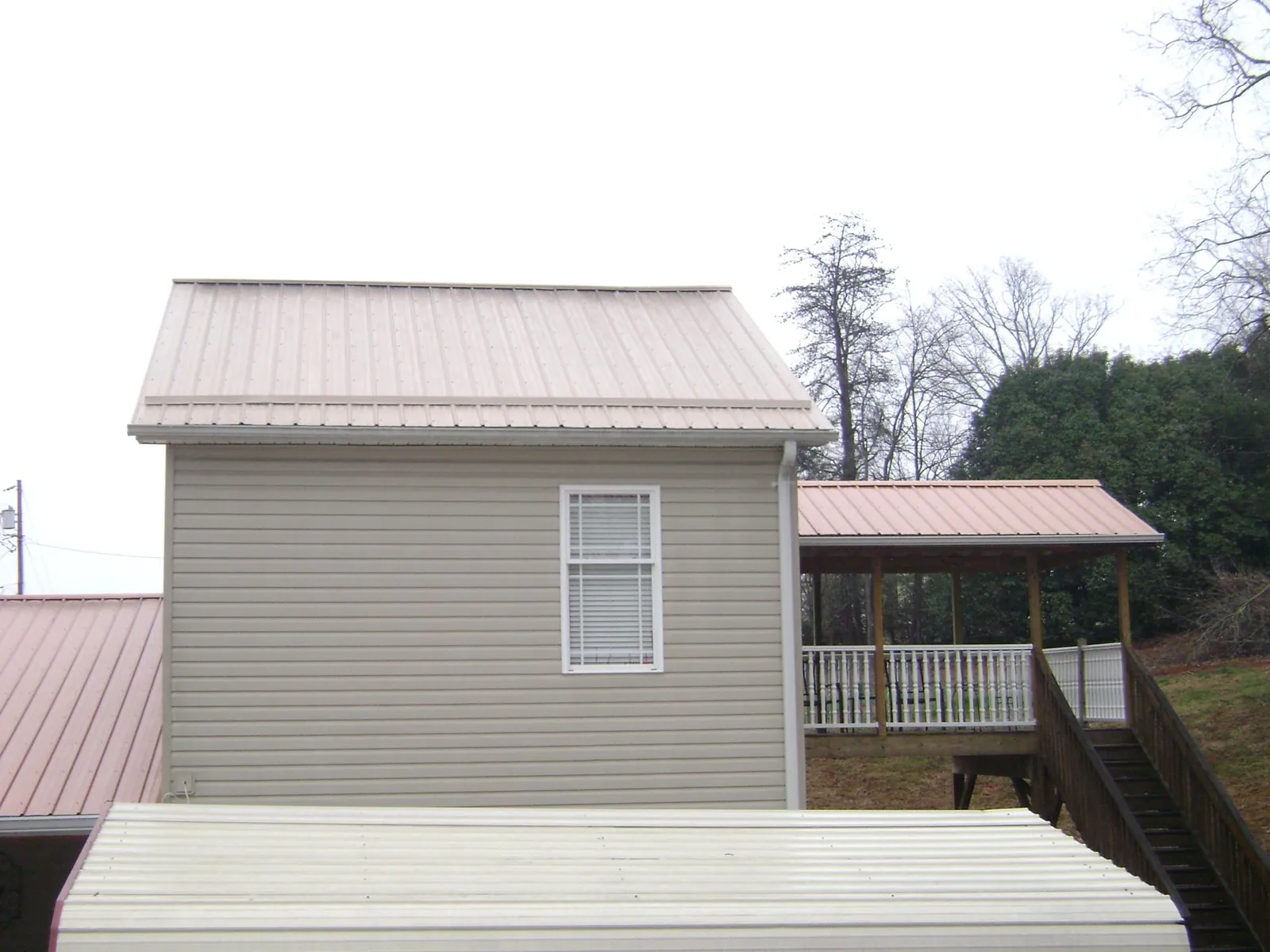 Tan metal roofs on a two story addition and attached porch, from a Roof Replacement job in Birmingham